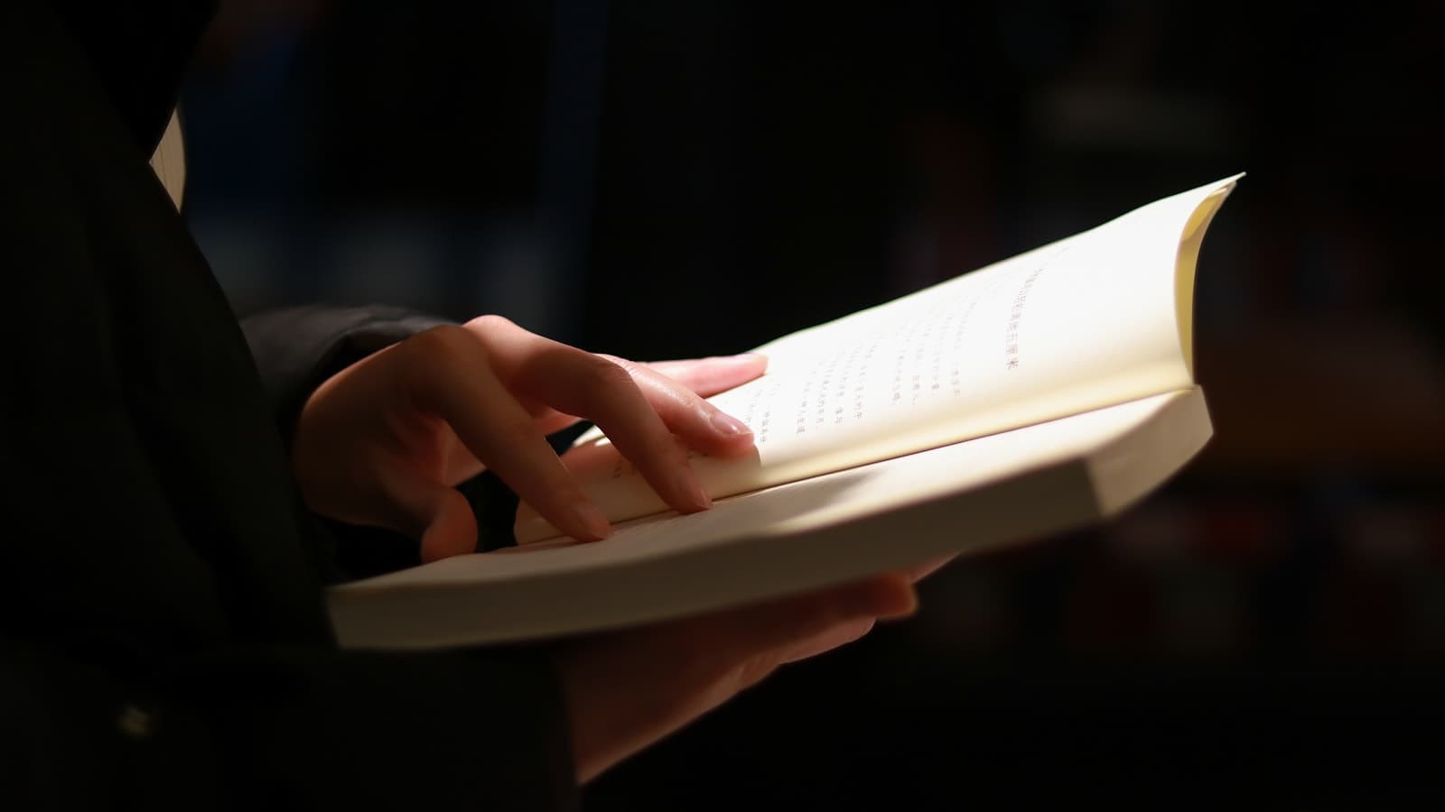 A pair of hands holding open a printed book in low directional light.