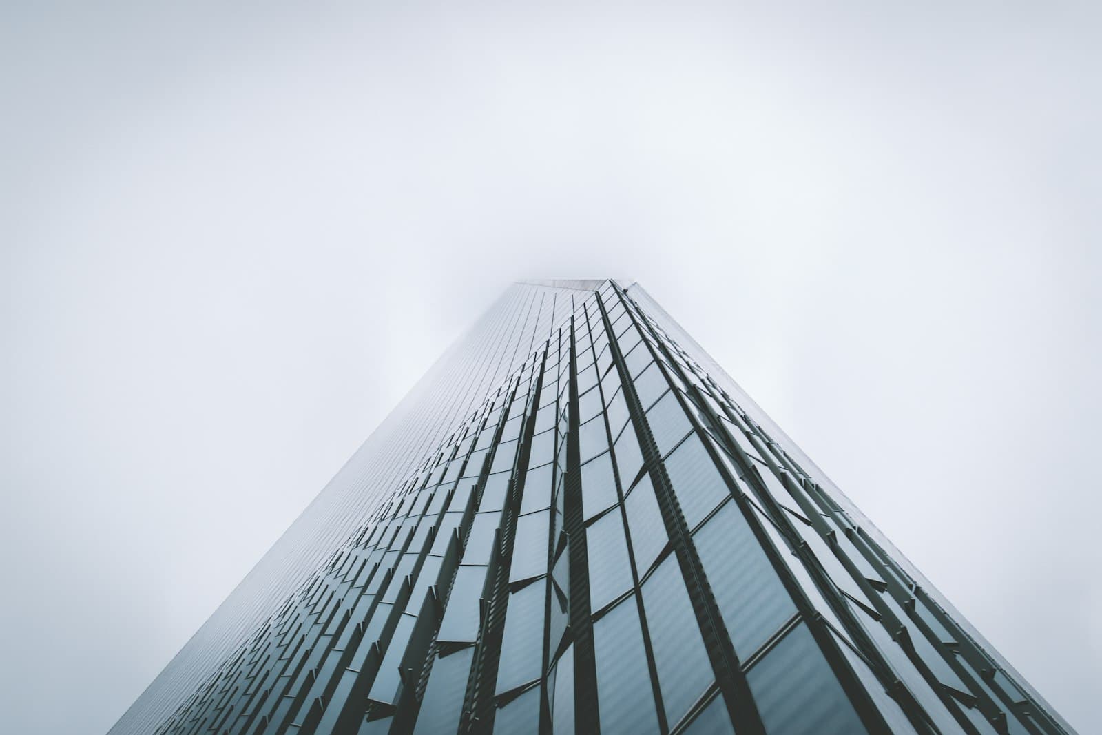 Single skyscraper photographed from below, its summit disappearing into a misty overcast sky.