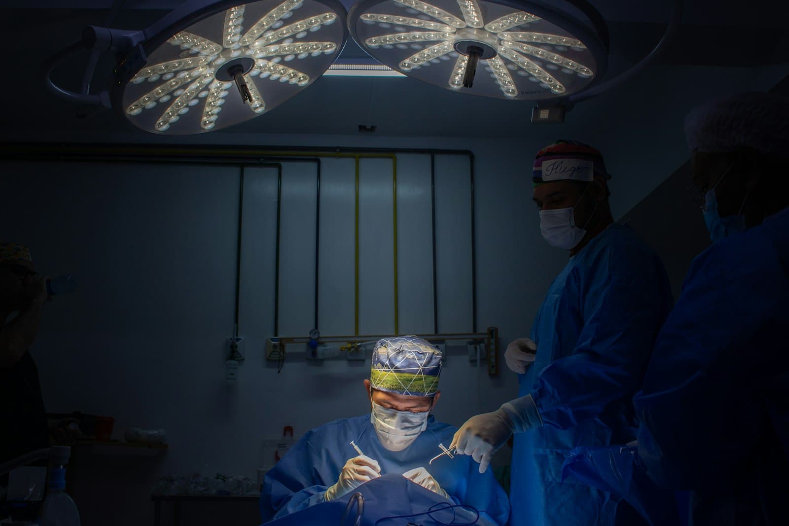 Operating theatre under bright surgical lights, masked clinicians working in low ambient light.