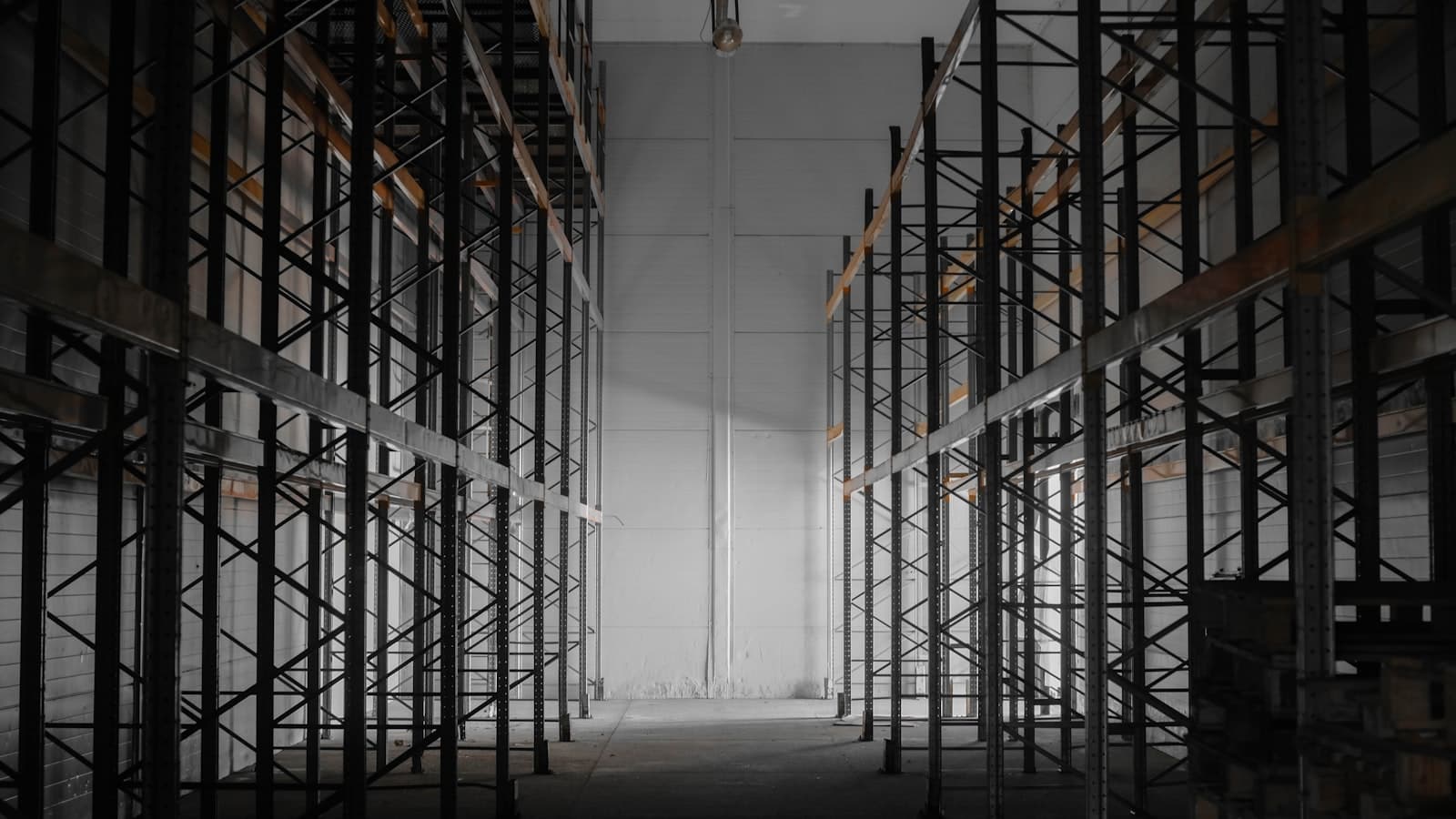 Empty industrial warehouse with rack framing converging toward a bright back wall.